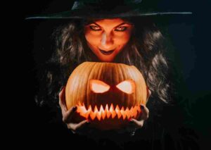 Mysterious black witch with pumpkin as head of jack-o-lantern on dark backdrop. Scary symbol of Halloween,